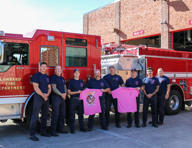 Group photo of Lombard Firefighters holding pink t shirts in front of red fire engine
